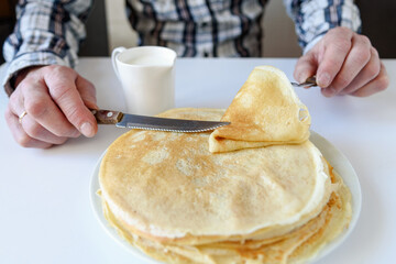 Men's hands hold milk and a pancake. There are a lot of pancakes on a white plate.