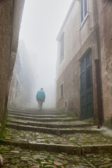 man walks up stairs in fog in small town