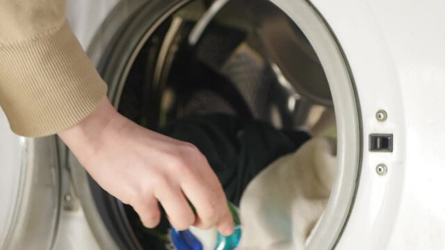 Hand put gel caps into washing machine. Household laundry equipment. Spring clothes cleaning.