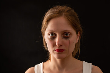 Blonde female with sad expression from front on black background. Young woman crying with blank look in darkenss. Upset female without smile in depression.