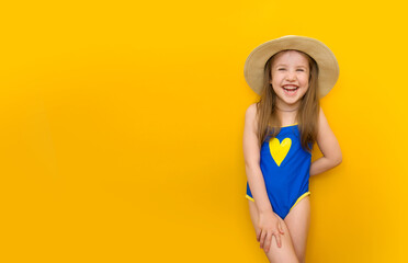 Happy little child in a blue swimsuit and a straw hat on a yellow background. Banner with a cute beautiful girl who laughs cheerfully. Beach vacation and summer vacation concept. Place for text