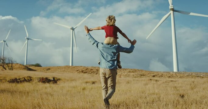Hopeful father carries son on his back to wind turbines while dreaming of a green renewable energy future, clean and sustainable energy, fighting climate change for future generations
