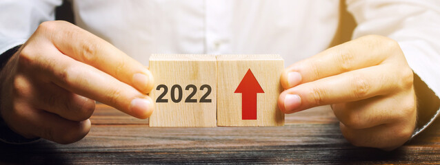 Businessman holds wooden blocks with the inscription 2022 and an up arrow. The forecast concept for...