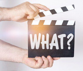 On a white background, a man holds a clapperboard in his hands on which it is written - WHAT