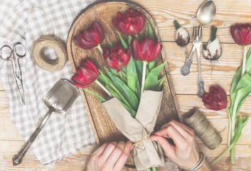 Top view of hands tying rope on red tulips bouquet in wrapping paper