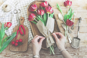 Top view of hands tying rope on red tulips bouquet in wrapping paper