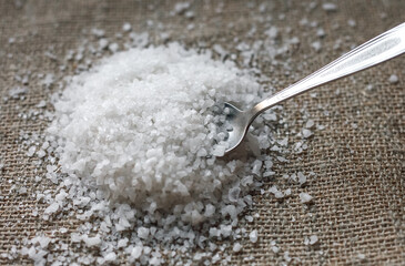 Crystals of coarse salt on the table.The spoon takes the salt.