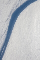Beautiful winter background with snowy ground. Natural snow texture. Wind sculpted patterns on snow surface. Closeup top view with copy space.