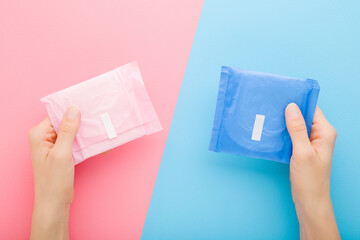 Young adult woman hands holding two packs of sanitary towel on light pink blue table background....
