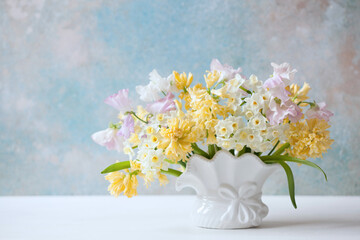 Bouquet in a vase of hyacinths, sweet pea flowers and daffodils on a decorative colored background. Closeup, blur, selective focus.