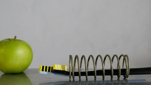 Two modern toothbrushes swing in a metal spring. Reflection on a steel surface. Green apple. 