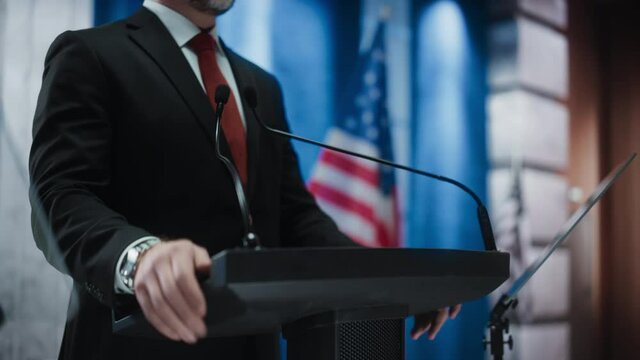 Close up of Organization Representative Speaking at a Press Conference in Government Building. Press Officer Delivering a Speech at a Summit. Minister at Congress. Backdrop with American Flags.