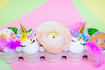 white Easter eggs decorated in the form of unicorns on a colorful background with ranunculus flowers, a minimal creative concept of a happy Easter