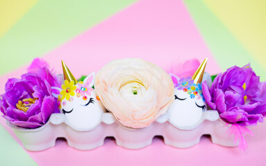 Obraz na płótnie Canvas white Easter eggs decorated in the form of unicorns on a colorful background with ranunculus flowers, a minimal creative concept of a happy Easter