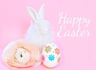 Ceramic Easter Bunny, white Easter egg and ranunculus flower on pink background and text Happy Easter, a minimal creative concept
