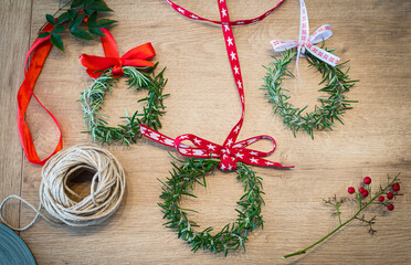 Fototapeta na wymiar Three rosemary wreaths decorated with red ribbons, on a wooden table. Natural home decor, diy, idea for Christmas. Top view, flat lay.