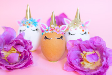white and brown Easter eggs decorated in the form of unicorns on a pink background with ranunculus and tulips flowers, a minimal creative concept of a happy Easter