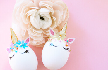 Fototapeta na wymiar white Easter eggs decorated in the form of unicorns on a pink background with ranunculus flower, a minimal creative concept of a happy Easter