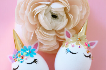 white Easter eggs decorated in the form of unicorns on a pink background with ranunculus flower, a minimal creative concept of a happy Easter