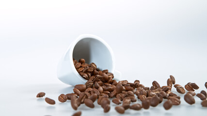 Spilled coffee beans from ceramic cup isolated over white background