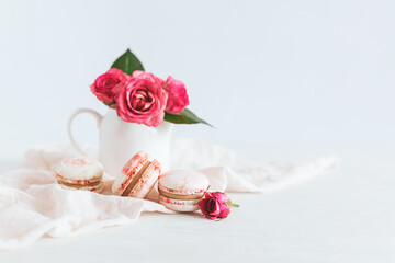 Tasty french macaroons with pink roses on a white background.