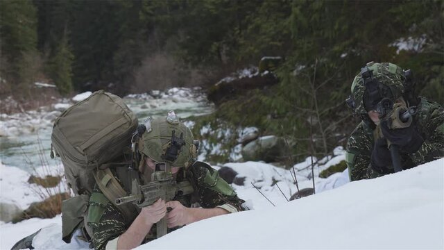 Army Man wearing Tactical Uniform and holding Machine gun in the Outdoor Rain Forest. Winter Warfare. Taken in British Columbia, Canada. Slow Motion. Taking cover in Snow