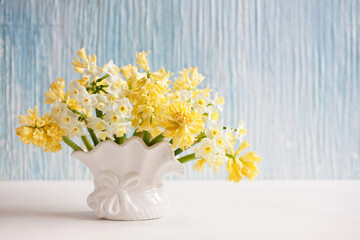 Bouquet of yellow hyacinths and daffodils in a vase on a table, blue background wall. Closeup, blur, selective focus.
