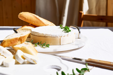 Delicious cheese brie or camembert on ceramic cutting board with herbs and baguette on the table...