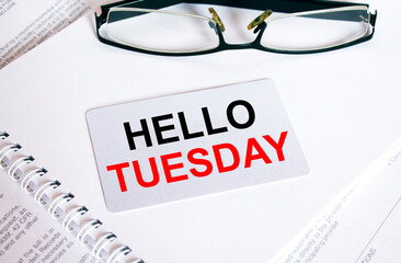 Text Hello Tuesday on a business card lying on a notepad with eyeglasses and text documents