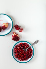 Fresh pomegranate seeds in plate with pomegranate slices on white table. 
