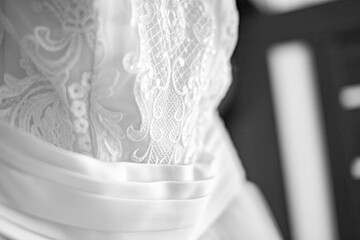 Black and white close - up photo of the waist on a white wedding dress with white embroidery. Wedding traditions.