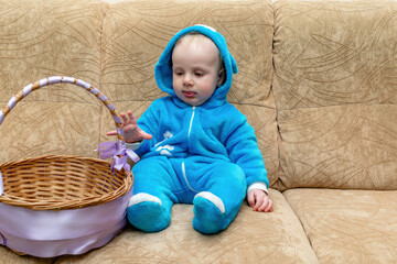 Naklejka premium Cute little baby toddler boy wearing rabbit costume with basket sitting on couch. Easter concept with copy space