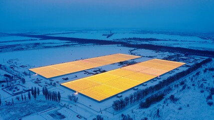 Aerial side view of large industrial greenhouses for growing plants in winter. light pollution. winter day at sunset. Flying along modern plantation glasshouse area. growing plants vegetables flowers