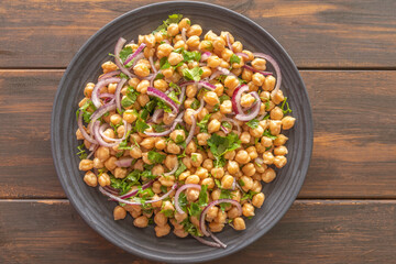 Chickpea Salad with Red Onion on dark plate over wooden background.