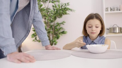 Irritated father talking to daughter, making child eat oatmeal in the morning