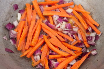 Carrot slices with red onions are fried in a cauldron on the grill