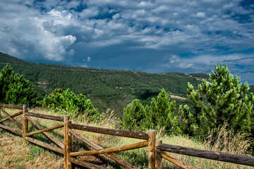 Fototapeta na wymiar Imagen realizada desde un mirador con vallas de madera y vegetación arbórea en dirección al bosque de montaña y nubes de tormenta