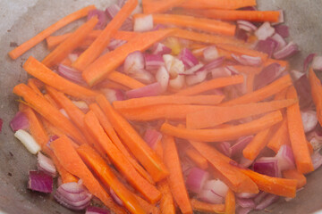 Carrot slices with red onions are fried in a cauldron on the grill