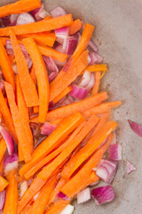 Carrot slices with red onions are fried in a cauldron on the grill