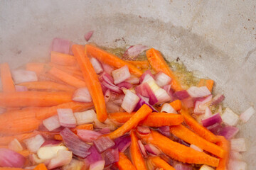 Carrot slices with red onions are fried in a cauldron on the grill