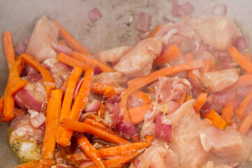 Chicken pieces are fried with carrots and red onions in a cauldron on the grill