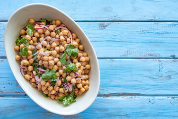 Chickpea Salad with Red Onion on blue wooden background with copy space.