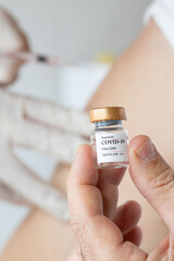 Vial  with COVID-19 vaccine in the hand of a vaccinated person. Medical assistant is administrating vaccine