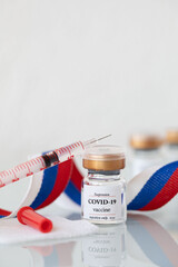 Vial  with COVID-19 vaccine and syringe. Closeup. Russian flag in the background