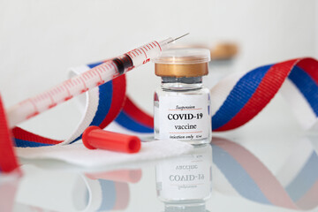 Vial  with COVID-19 vaccine and syringe. Closeup. Russian flag in the background