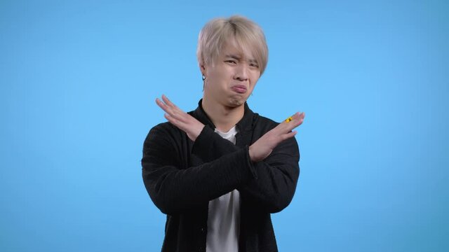 Portrait of serious korean man disapproving with no crossing hands sign make basta, negation, enough gesture. Denying, Rejecting, Disagree. Portrait of handsome asian guy on blue background