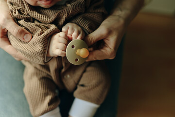 baby holds a pacifier in his mother arms