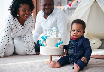 happy one year old baby boy with birthday cake and happy parent on the background