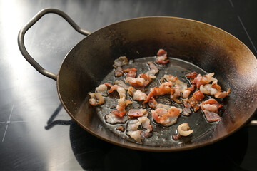 Crispy chopped bacon pieces fried in an iron pan on the black stove, copy space, selected focus