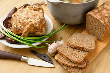 baked meat, soup and blood sausage on a plate, green onion and garlic on wooden background, home...